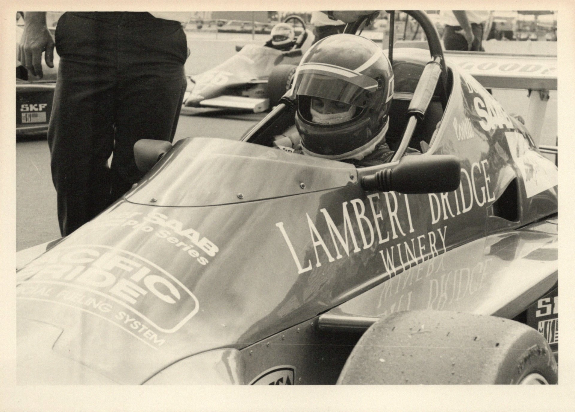 Helmeted driver in the team's open-wheel car, from the team's black-and-white archive